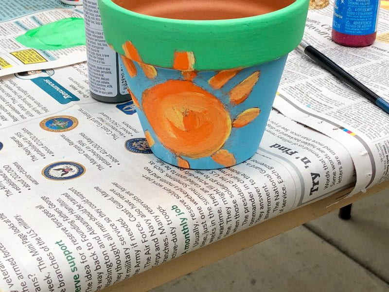 clay pot with painted sun design on newspaper