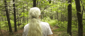 back view of head and shoulders of a person with long gray ponytail walking down a wooded path